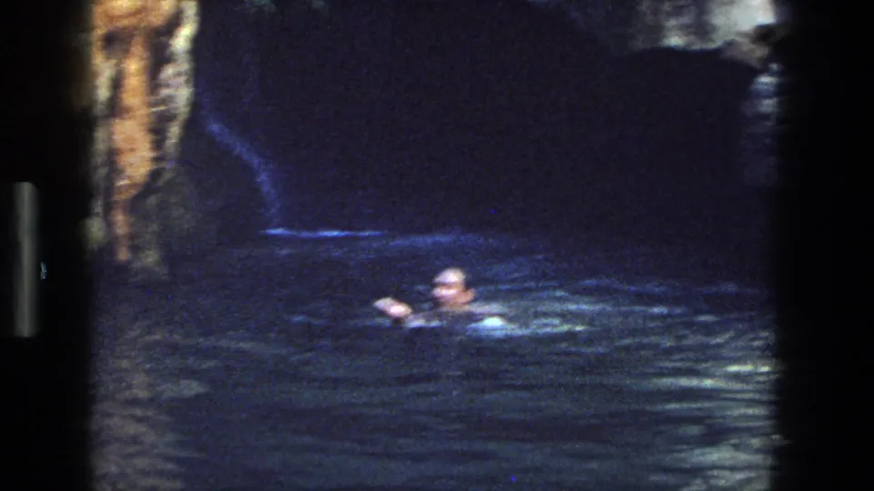 A swimmer moves through a dark rocky pool in archival 8mm footage from the Utah 1969 clip.