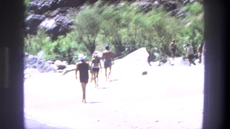 Several people walk across sunlit tan sand near shrubs and boulders in the Utah 1969 home-movie clip.