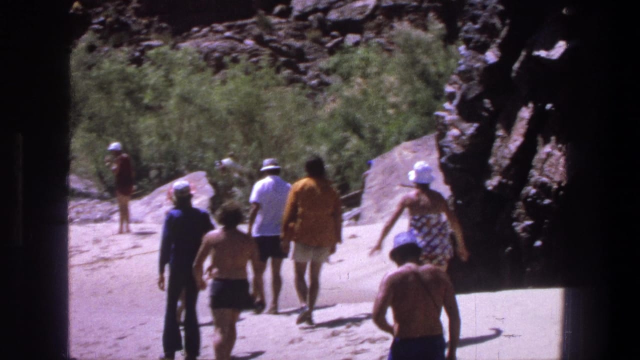 1969 Utah 8mm frame showing people in swimwear and hats walking from shade toward a sandy canyon path.