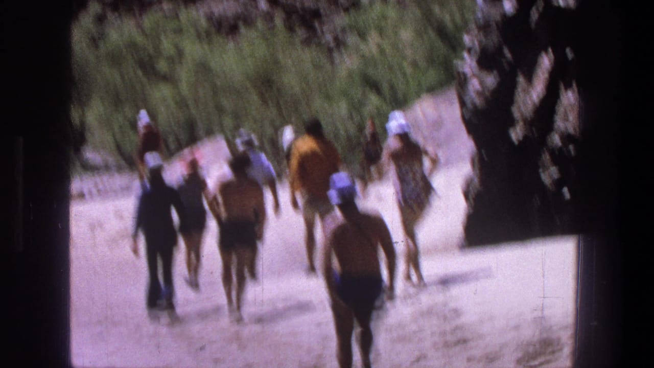 Distant walkers on a sandy path between canyon rock and shrubs.