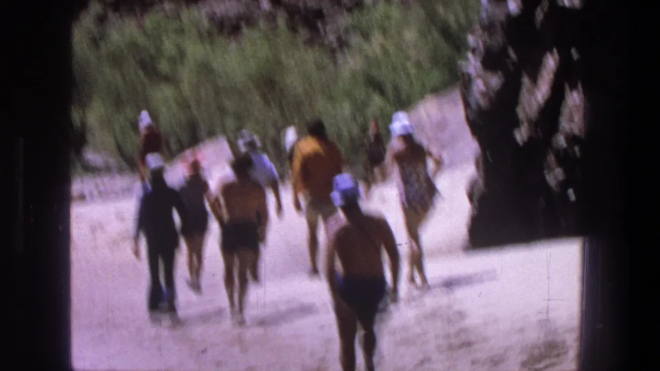 Soft 8mm frame of a group walking through a sunlit Utah canyon path, seen from behind and at a distance.