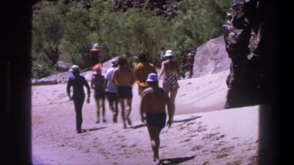 1969 Utah home-movie frame with visitors in hats, shorts, and swimwear walking away on pale sand.