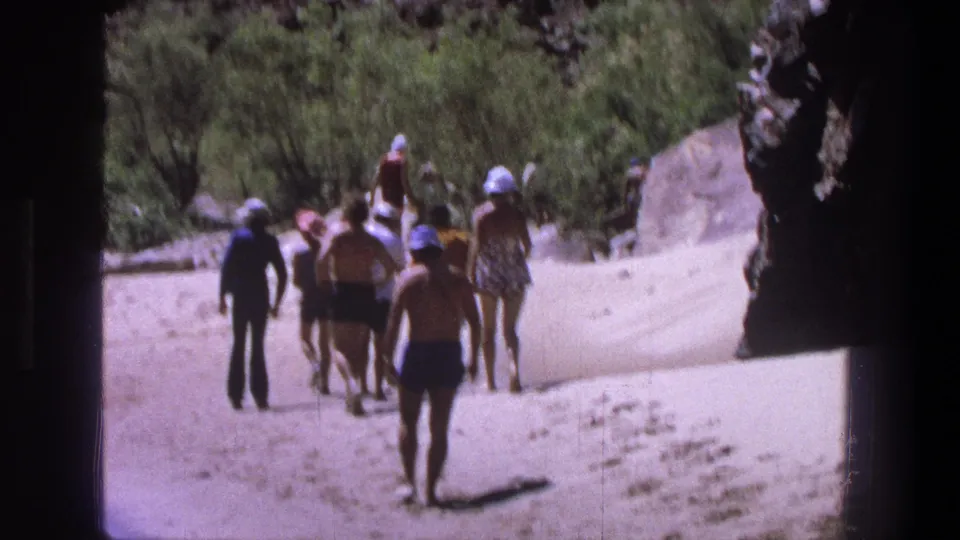 Late-1960s Utah 8mm still of a casual group walking through a sunlit sandy canyon corridor.