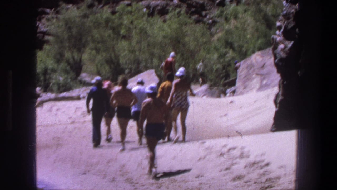1969 Utah 8mm frame of adults in swimwear and hats walking away on a sandy path near rocks and brush.