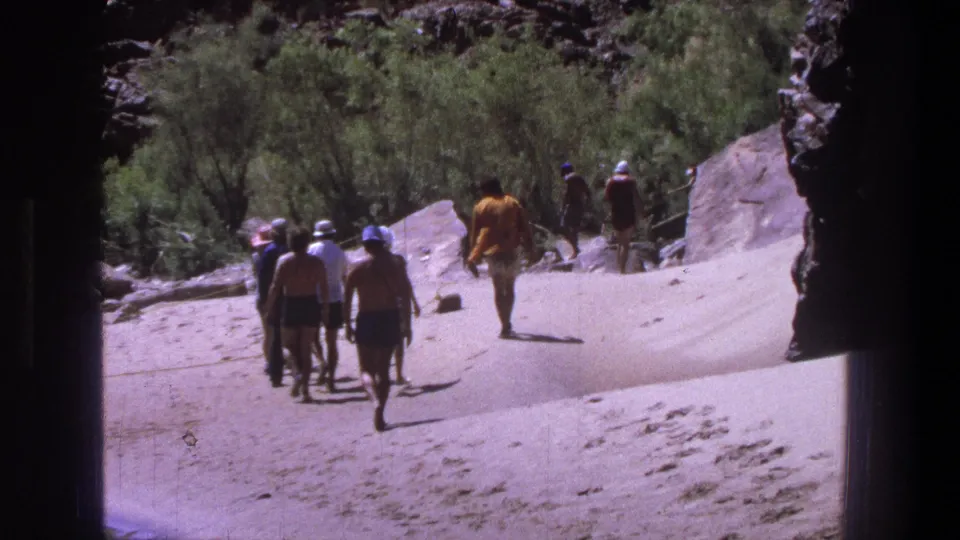 1969 Utah 8mm still of a small group in swimwear walking through a sandy, rocky outdoor setting with shrubs nearby.