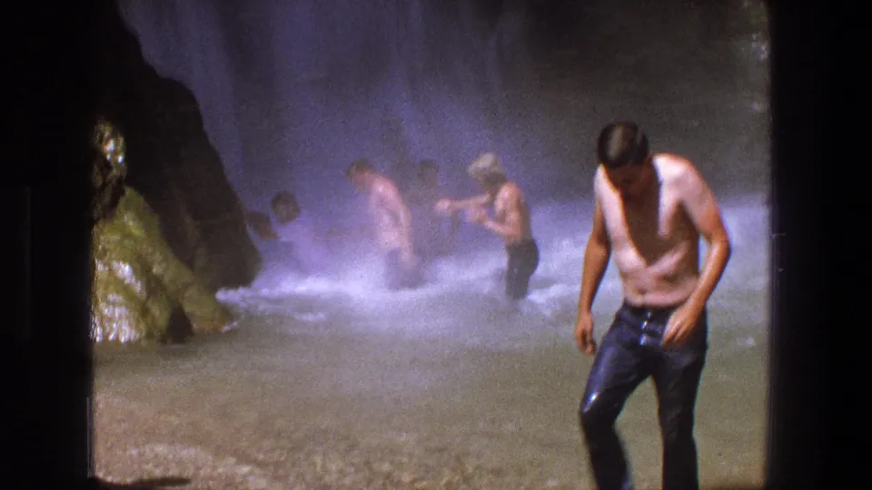 A shirtless man in wet dark pants walks toward the camera while other men remain in waterfall mist behind him, consistent with 1969 Utah metadata.