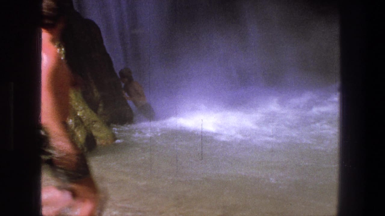 1969 Utah frame with a shirtless man in patterned trunks crossing the foreground near waterfall spray and rocks.