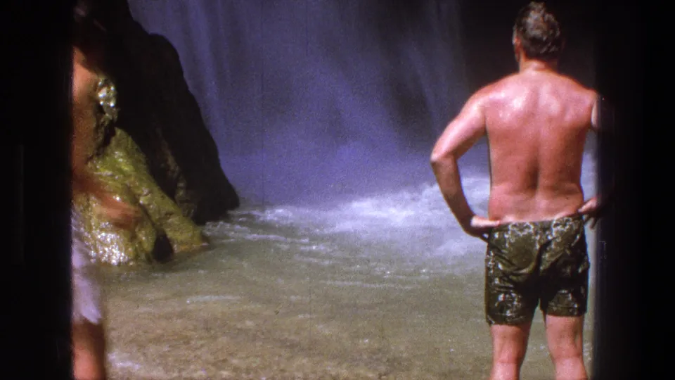 1969 Utah frame showing a man from behind standing near turbulent waterfall water in a rocky setting.