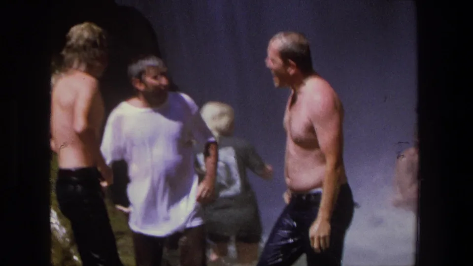 Three adult men, including one in a soaked white T-shirt and two shirtless men, stand close together near waterfall mist in Utah.