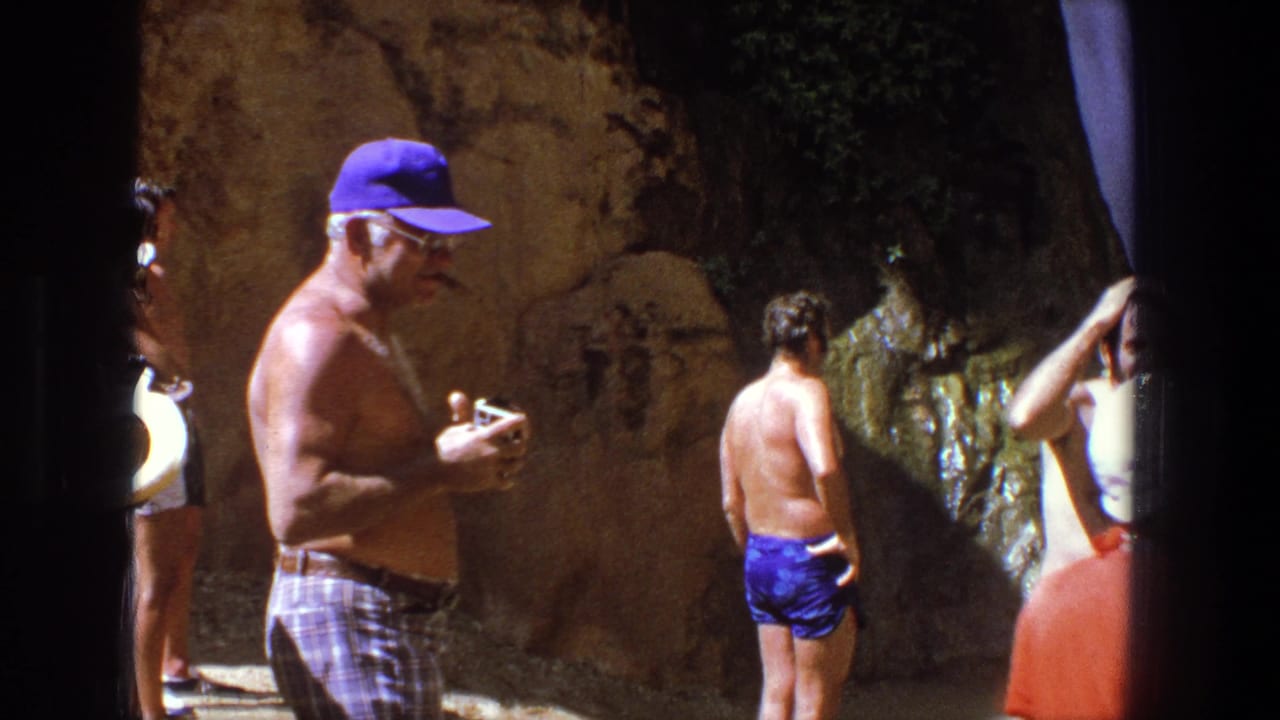 1969 Utah 8mm frame showing adults in swimwear gathered by wet canyon rock and shallow water at a natural recreation spot.