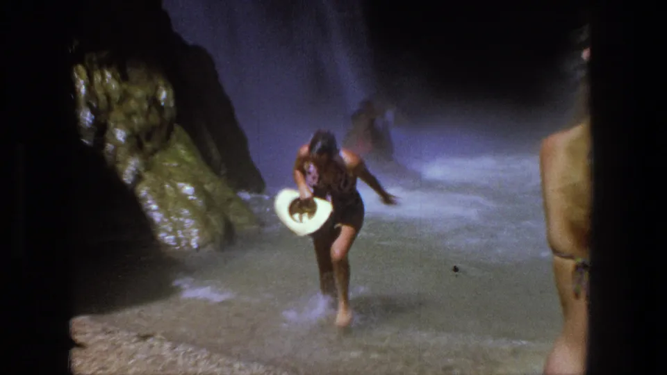 1969 Utah home-movie frame with swimmers wading through a rocky waterfall pool and a foreground figure partly blocking the view.