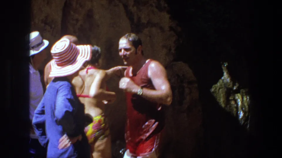 A small group in 1960s swimwear stands close together by the rocky waterfall area in Utah home-movie footage.