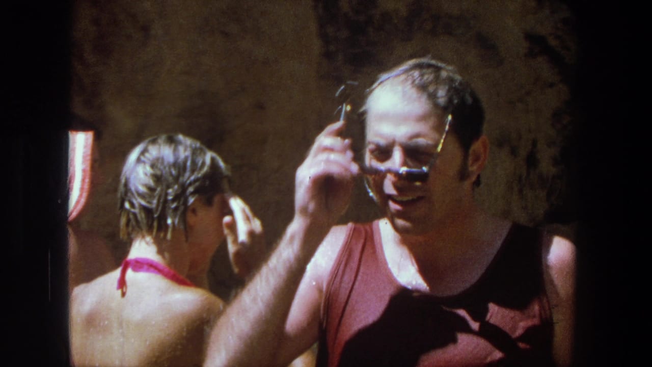 1969 Utah home-movie frame of a wet man adjusting sunglasses while a woman with wet hair stands nearby after swimming.