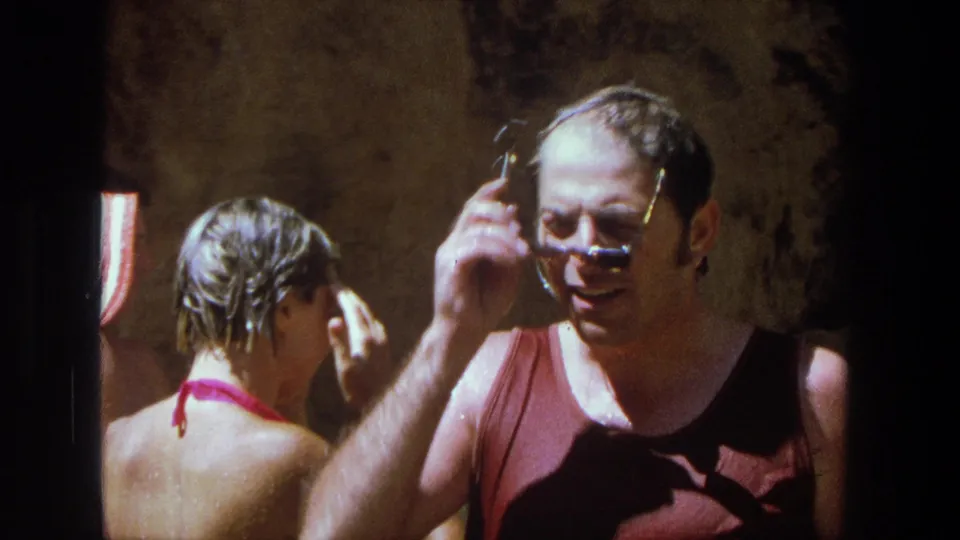 1969 Utah home-movie frame of a wet man adjusting sunglasses while a woman with wet hair stands nearby after swimming.