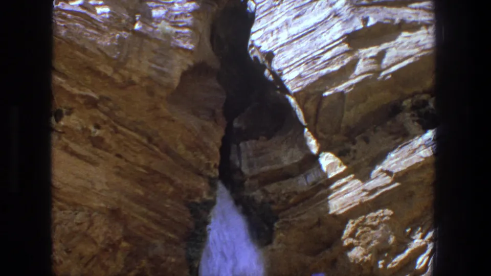 1969 Utah home-movie frame of a narrow waterfall spilling down between rugged sunlit rock faces.