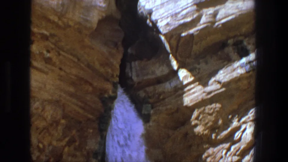 1969 Utah home-movie frame showing water cascading through a dark cleft in layered rock.