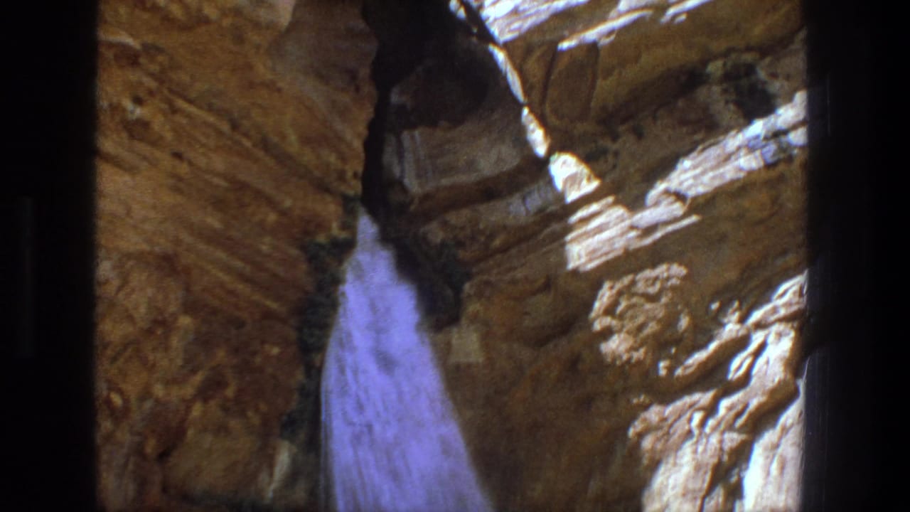 Waterfall dropping through tan rock walls with dark film borders.