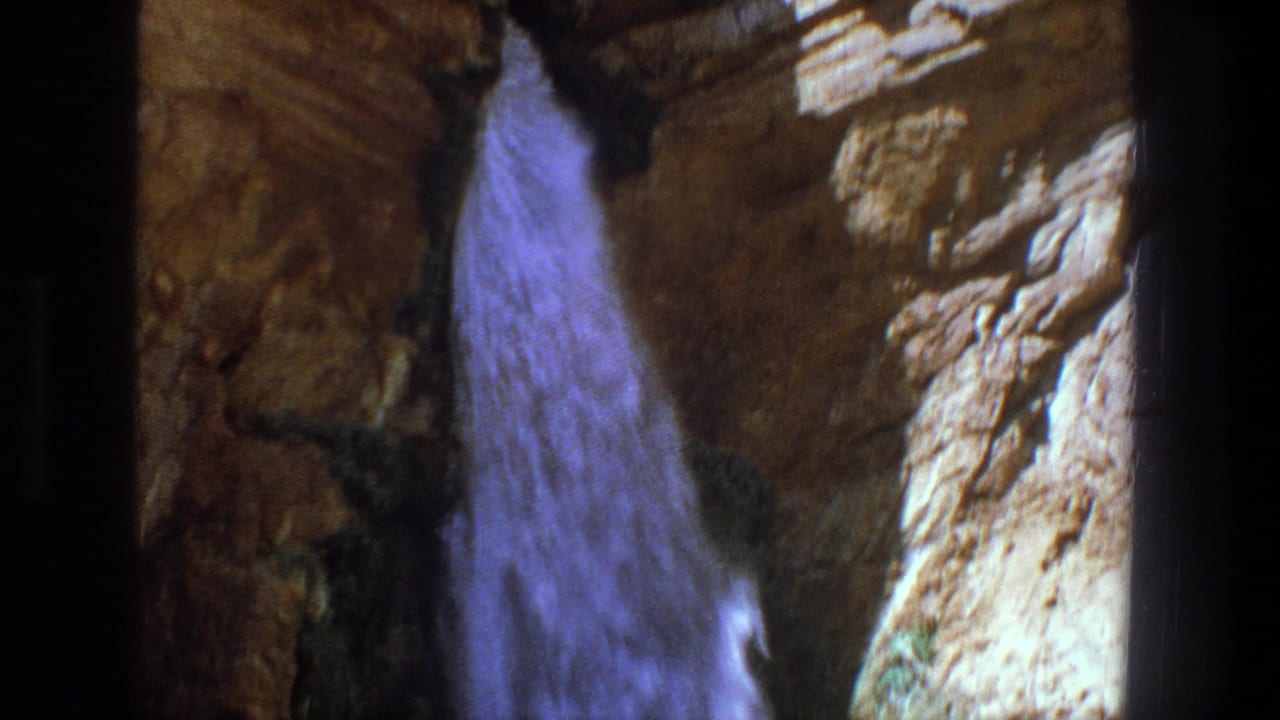 1969 Utah home-movie frame with a blue-toned waterfall flowing past textured canyon rock.