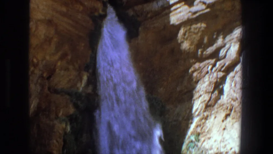1969 Utah home-movie frame with a blue-toned waterfall flowing past textured canyon rock.
