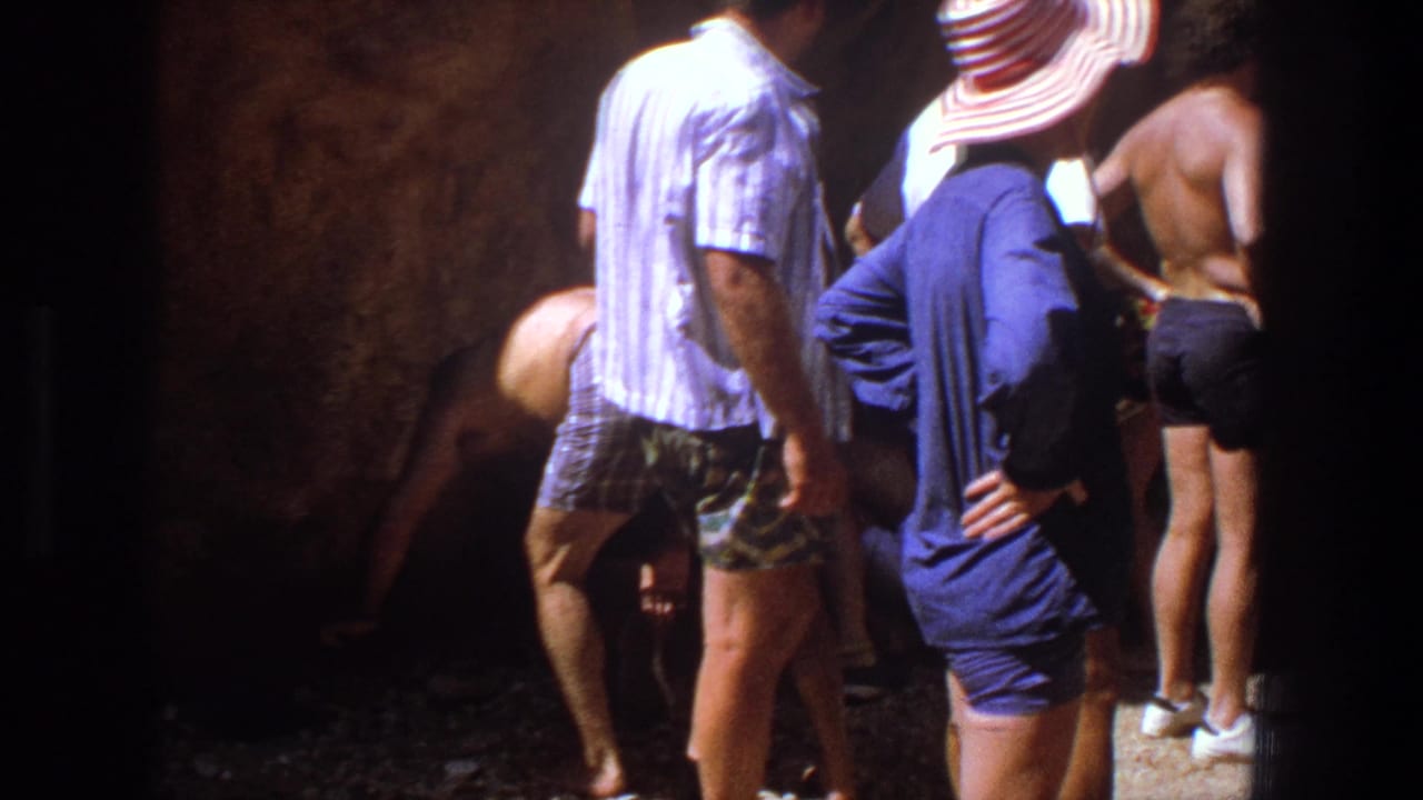 1969 Utah frame of adults gathered in a shaded natural rock space, partly backlit by bright sun outside the frame.