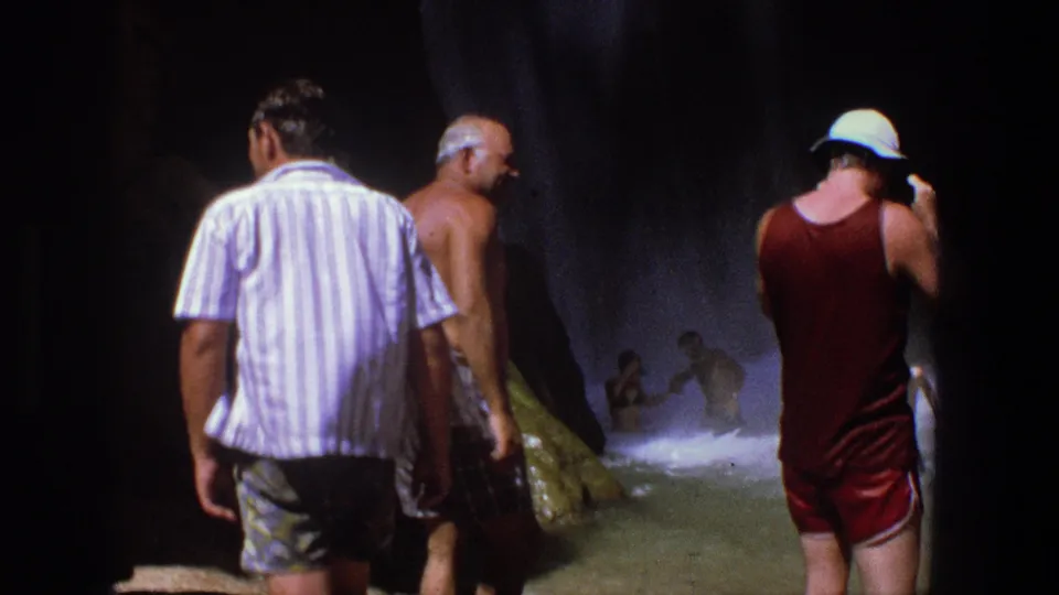 1969 Utah 8mm frame of adults moving through a dim cave, with a woman in red swimwear at the right edge.