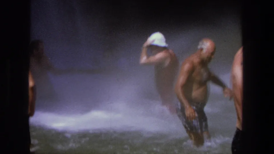 1969 Utah 8mm frame of adults wading in a waterfall pool, with foamy water, spray, and a white hat visible through the mist.