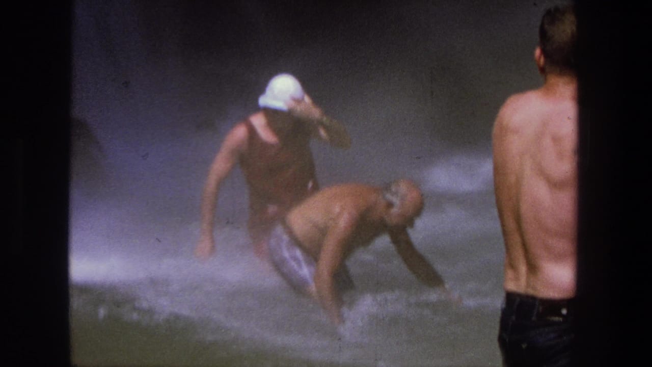 1969 Utah 8mm frame showing men in a misty waterfall pool, with one man bending into the rushing water and another watching from shore.