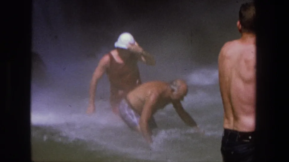 1969 Utah 8mm frame showing men in a misty waterfall pool, with one man bending into the rushing water and another watching from shore.