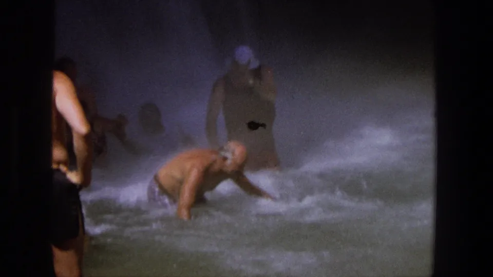 Misty 1969 Utah 8mm frame showing a man bracing in a waterfall pool while another person stands partly obscured by spray.