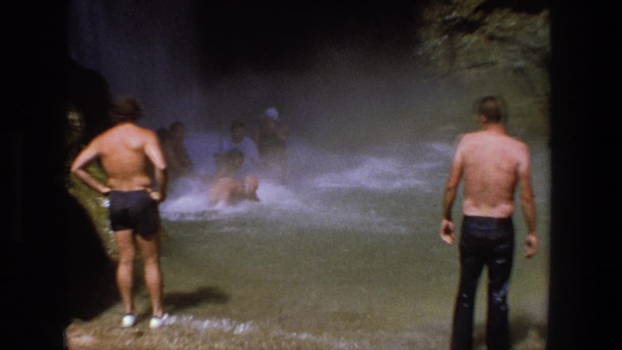 1969 Utah 8mm frame showing men in swimwear standing and wading in shallow water below a misty waterfall.