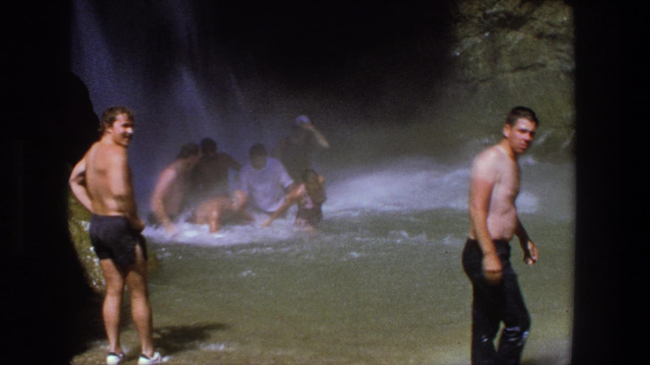 1969 Utah home-movie frame with men in swim trunks standing in and near rushing water at a waterfall base.