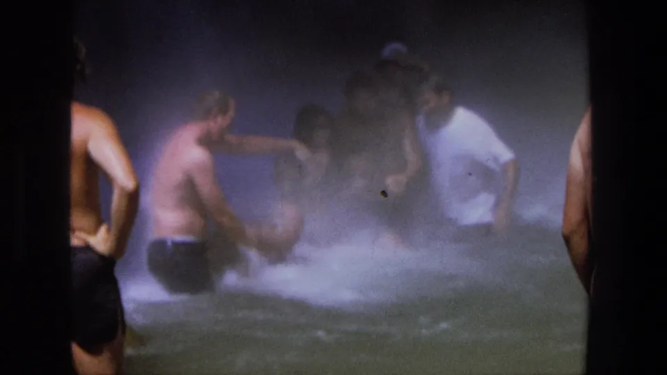 1969 Utah home-movie frame showing men gathered in churning waterfall water, with spray and soft focus across the scene.