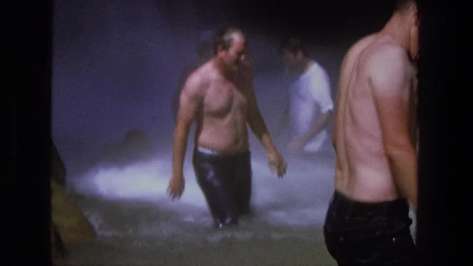 1969 Utah 8mm frame with a man walking through waterfall spray as other men stand in the pool and along the edge.