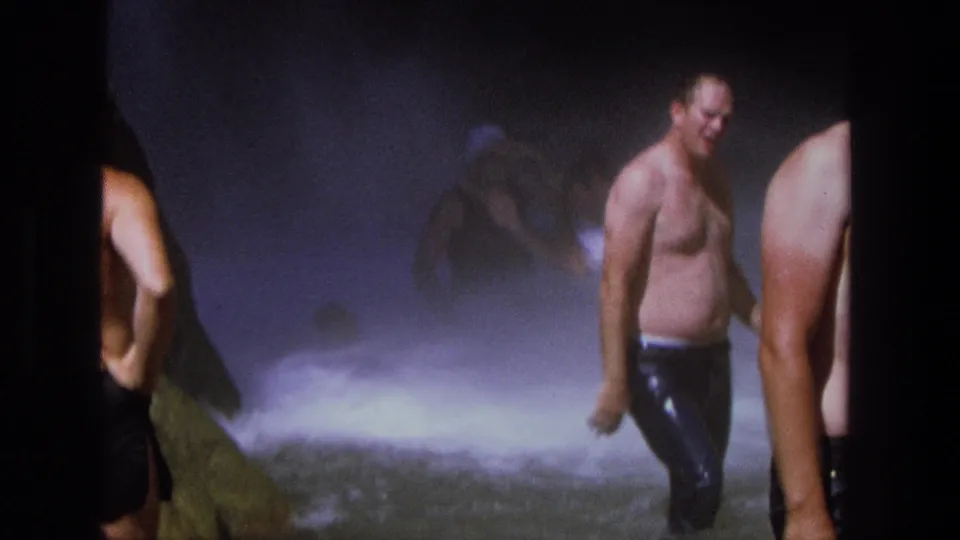 1969 Utah home-movie frame of adult men in swim trunks at the base of a waterfall, partly obscured by spray.