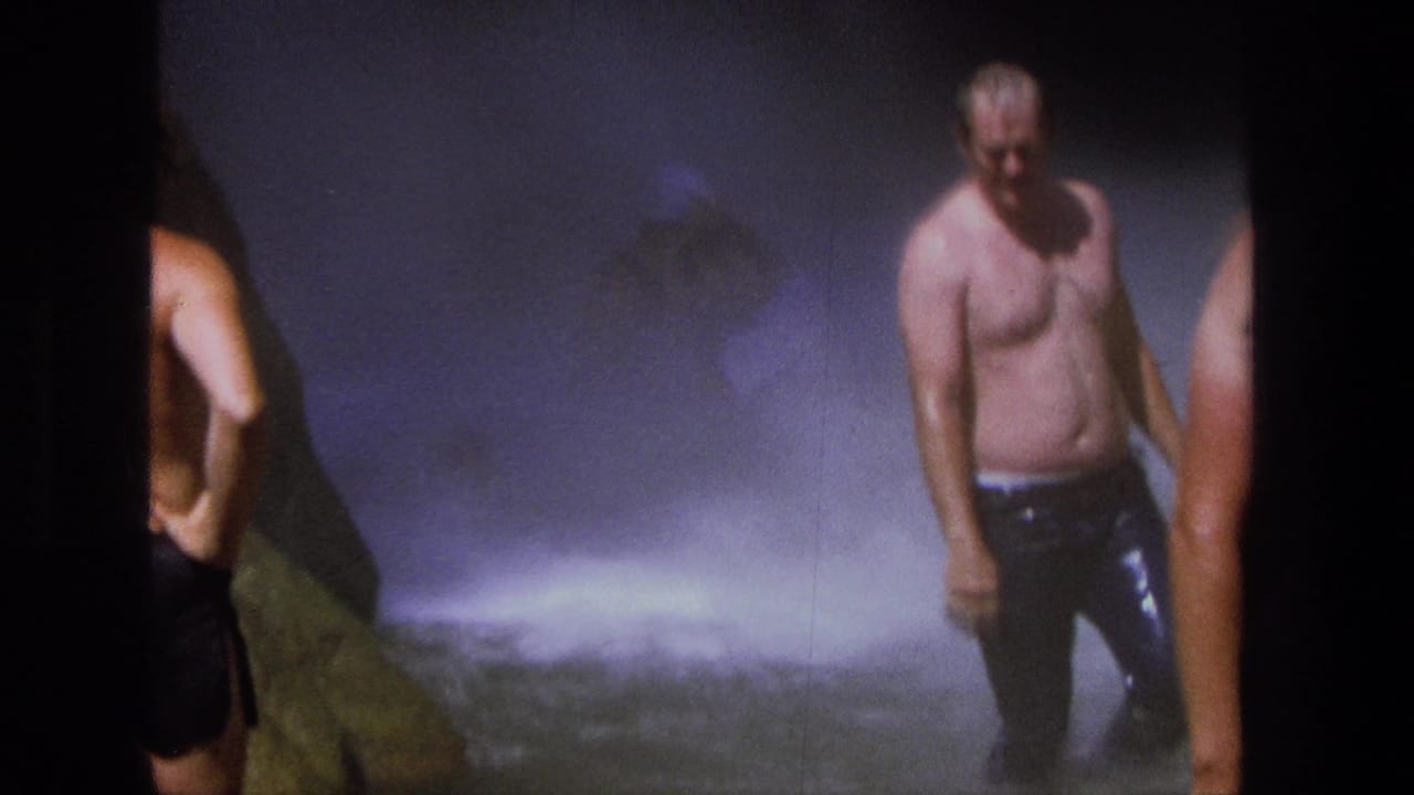 1969 Utah home-movie frame showing men in swim trunks near heavy waterfall spray and wet rock.