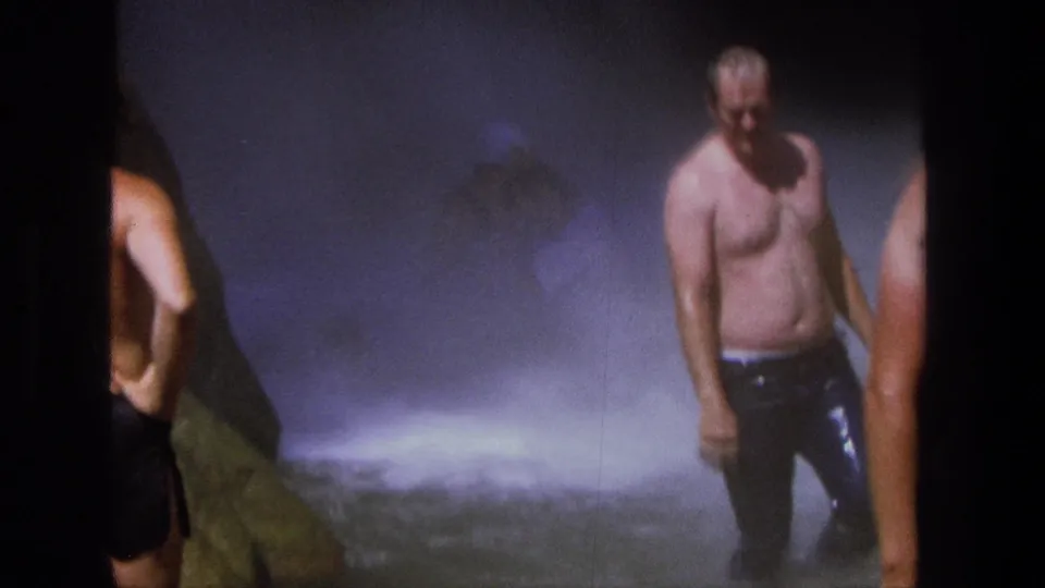 1969 Utah home-movie frame showing men in swim trunks near heavy waterfall spray and wet rock.