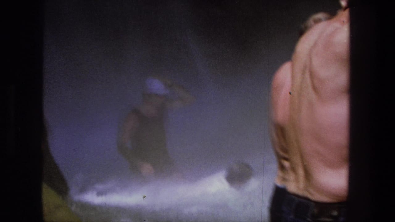 Men in waterfall spray with a shirtless figure close to the camera.