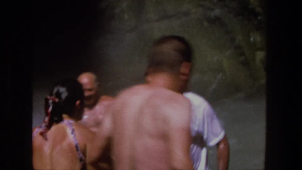In Utah 1969 home-movie footage, adults gather at the base of a waterfall, partly obscured by mist and handheld framing.