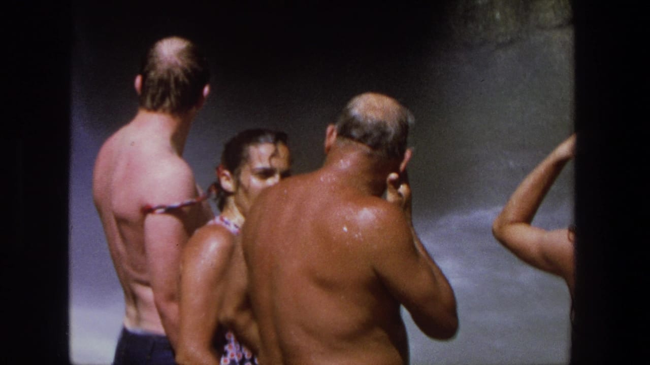 Group of swimmers faces waterfall spray beside a dark pool wall.