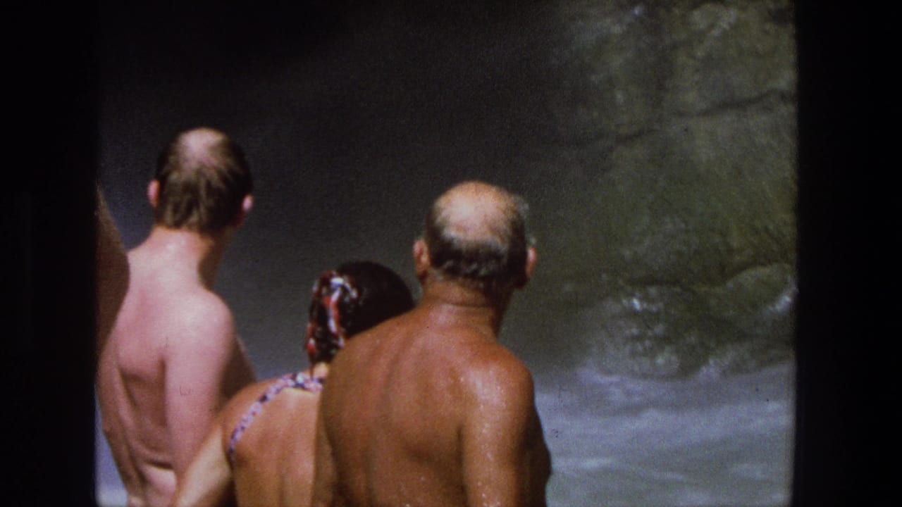 In Utah 1969 home-movie footage, three adults in swimwear face a rocky waterfall area with their backs mostly to the camera.