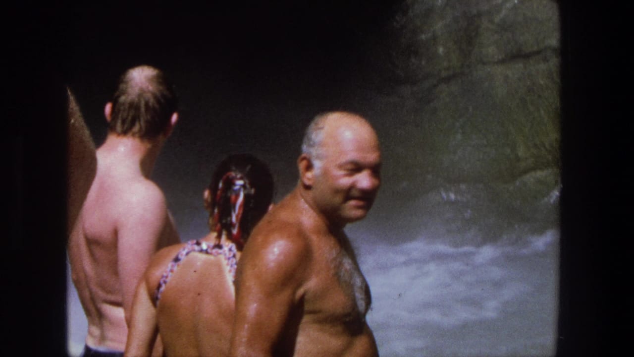 An older wet man turns toward the camera beside two other swimmers.