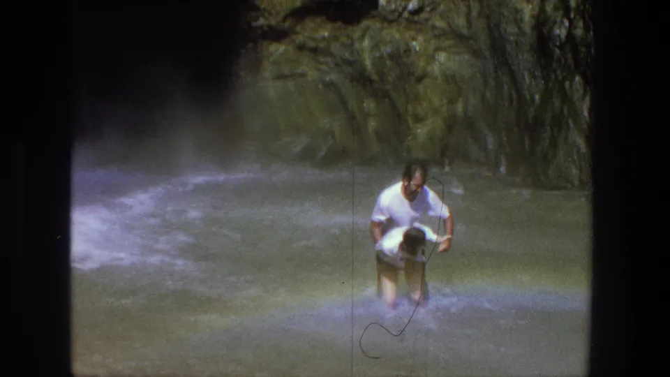 Two adults wade together through shallow water beneath a rocky Utah waterfall in this 1969 vacation footage.