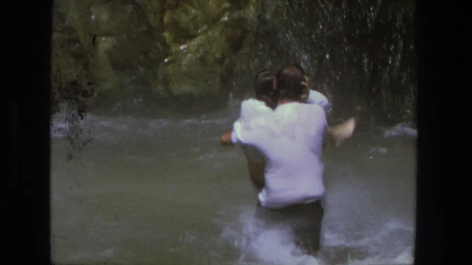 The couple appears from behind in a shallow Utah canyon stream, framed by dark 8mm film borders.