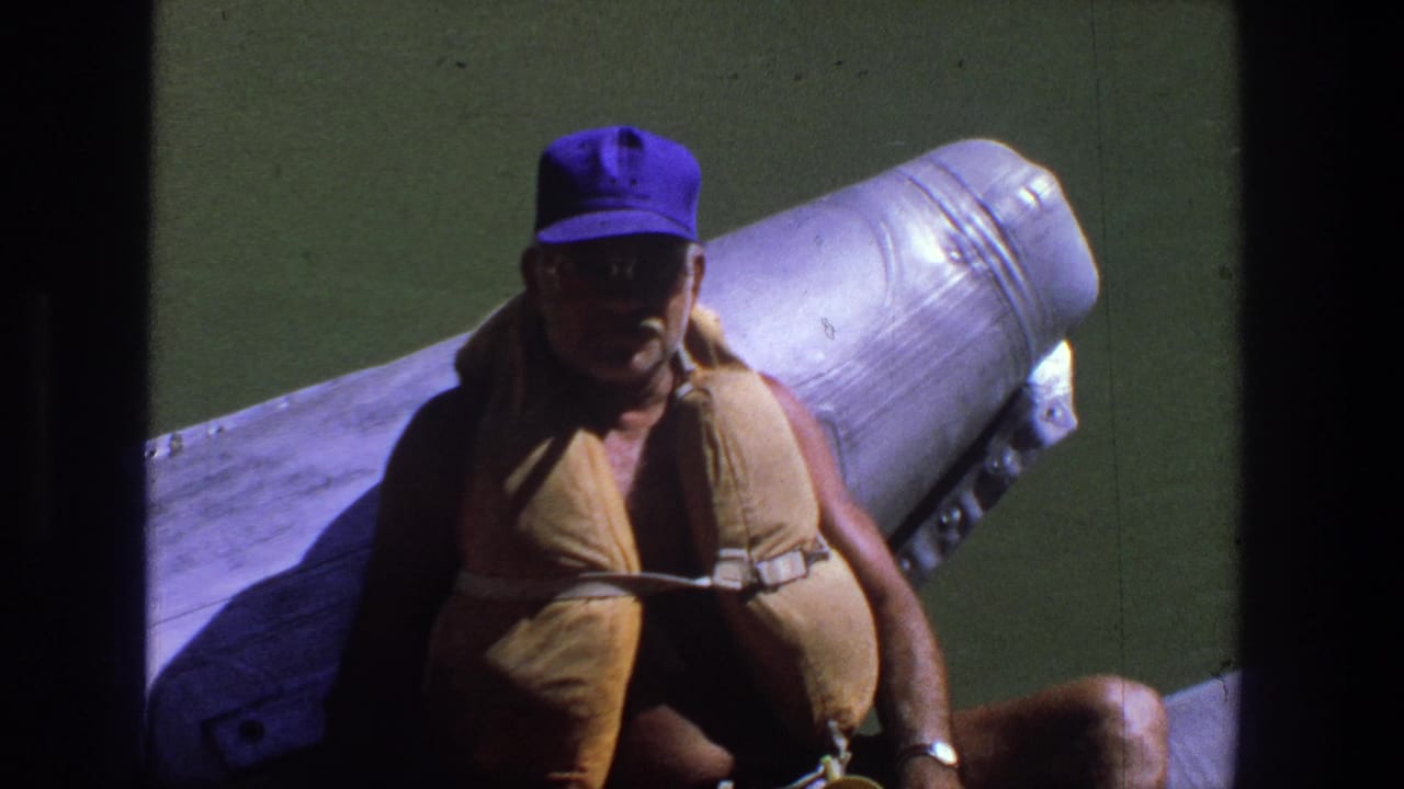 Man facing the camera on a boat, wearing sunglasses, cap, and life jacket.