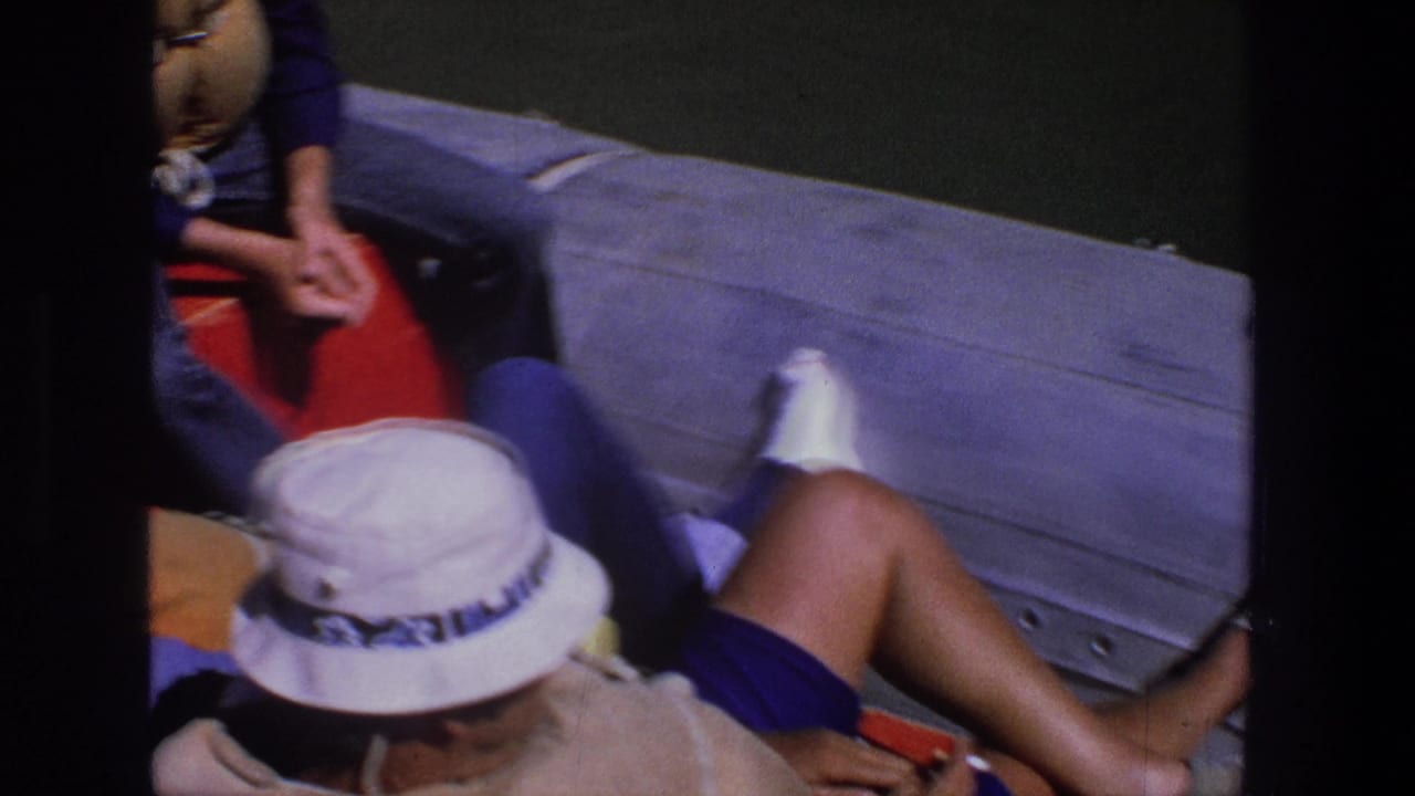 Adults relaxing on a red boat cushion, including a man in a white hat and sunglasses.