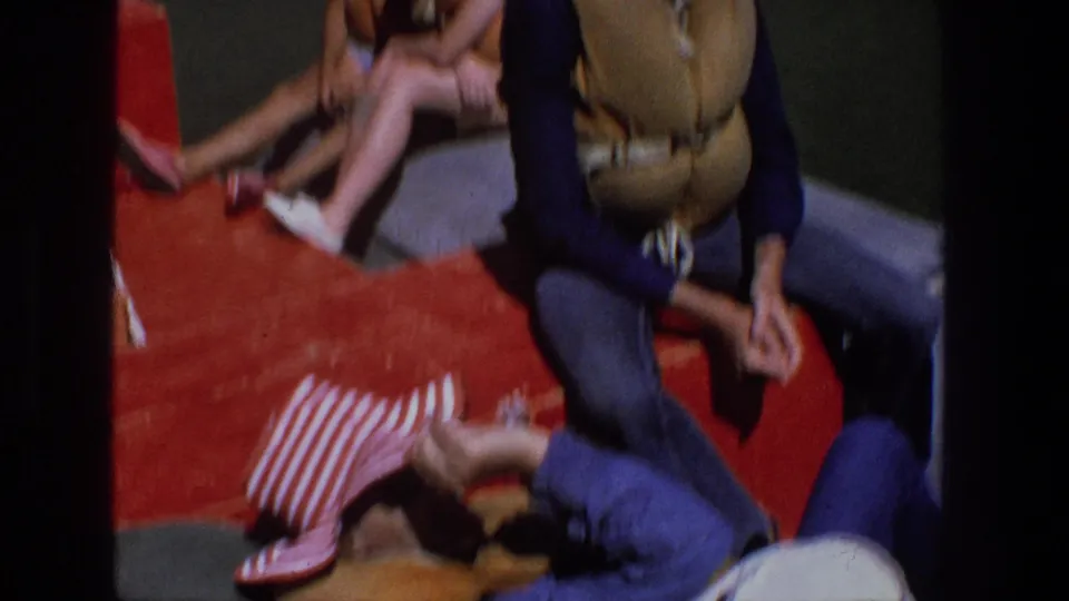 1969 Utah frame showing a person with a tan backpack seated on a red boat cushion as others relax nearby.