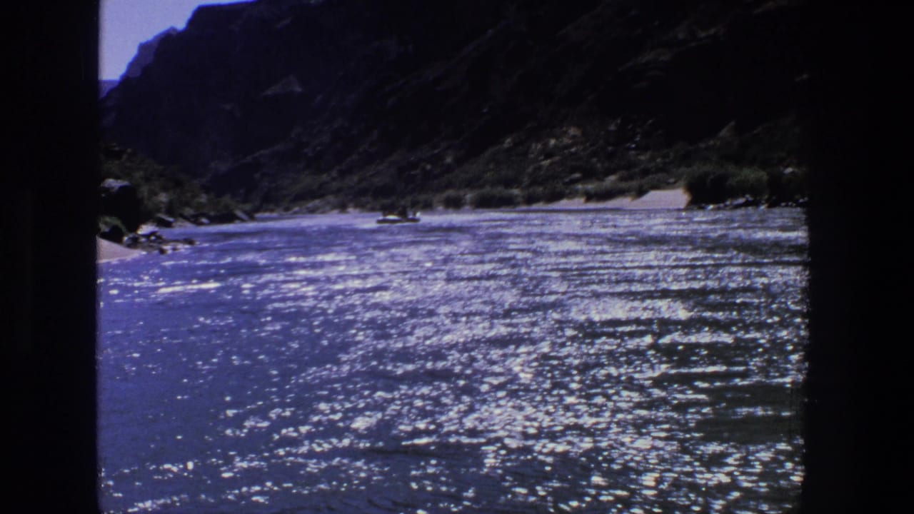 1969 Utah 8mm frame showing a sunlit canyon river, reflective water, sandy banks, and a small distant boat that may contain people.