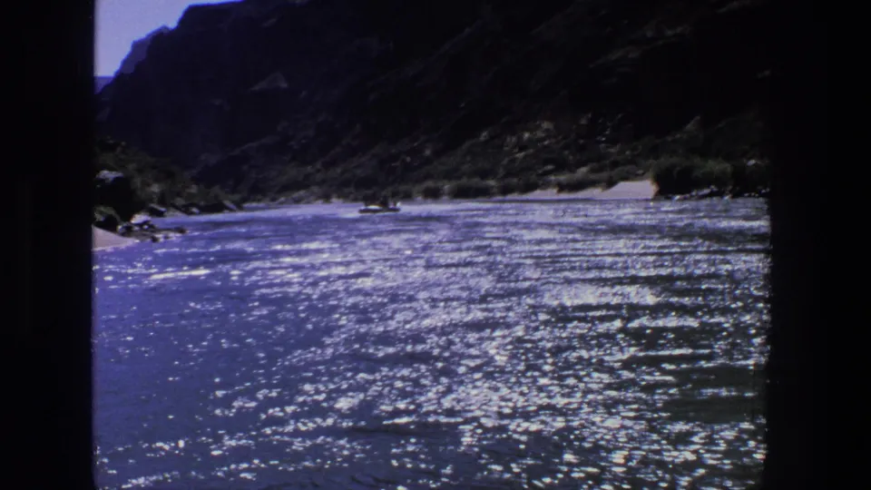 1969 Utah 8mm frame showing a sunlit canyon river, reflective water, sandy banks, and a small distant boat that may contain people.