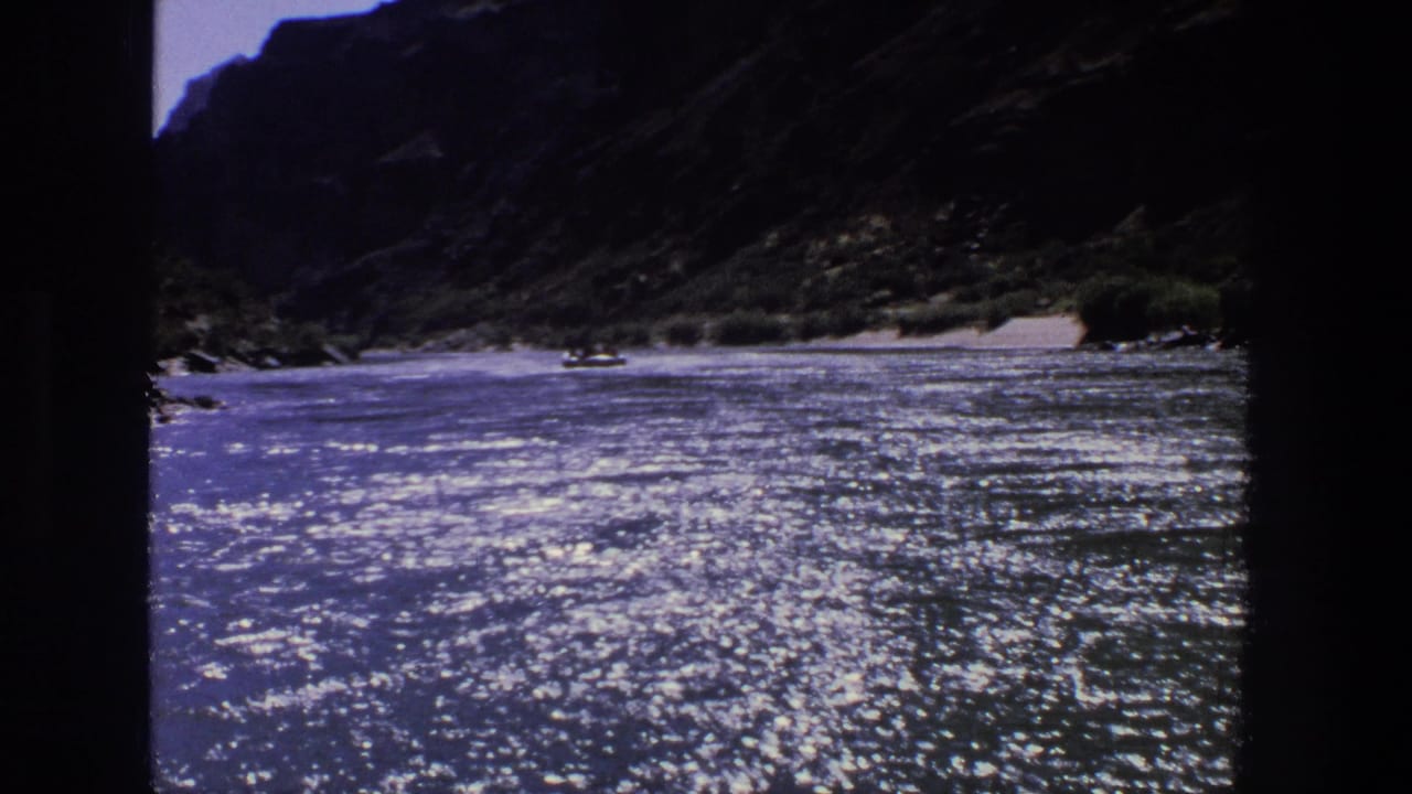 Blue river water sparkling below dark canyon slopes with a small distant boat.