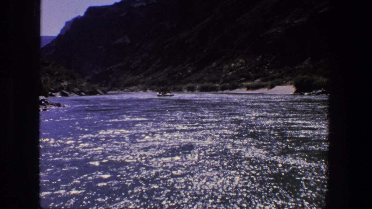 Wide river canyon view with glittering water, steep slopes, and a distant boat.
